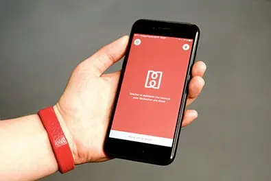 Une main porte le bracelet rouge HELP et tient un iPhone affichant l’application.